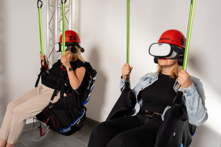 Besucherinnen mit VR-Brillen in aufgehängten Sitzen in der Triberg VR-Arena - Bild: Triberg VR-Arena