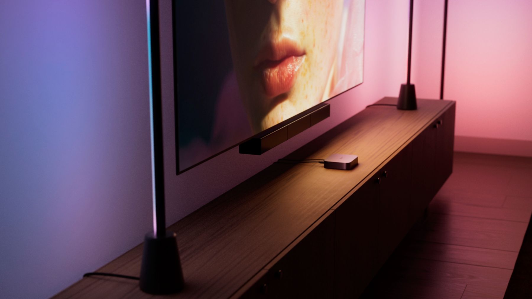 Hue Play HDMI Sync Box 4K vor einem Fernseher mit farblich synchronisierten Leuchten