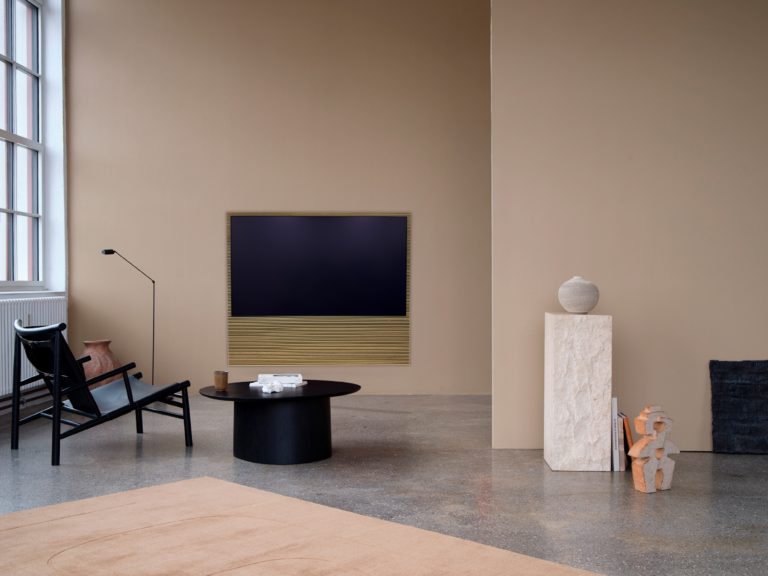 Samsung S99H OLED mit CANVAS-Soundbar und Holzlamellen an einer Wohnzimmerwand