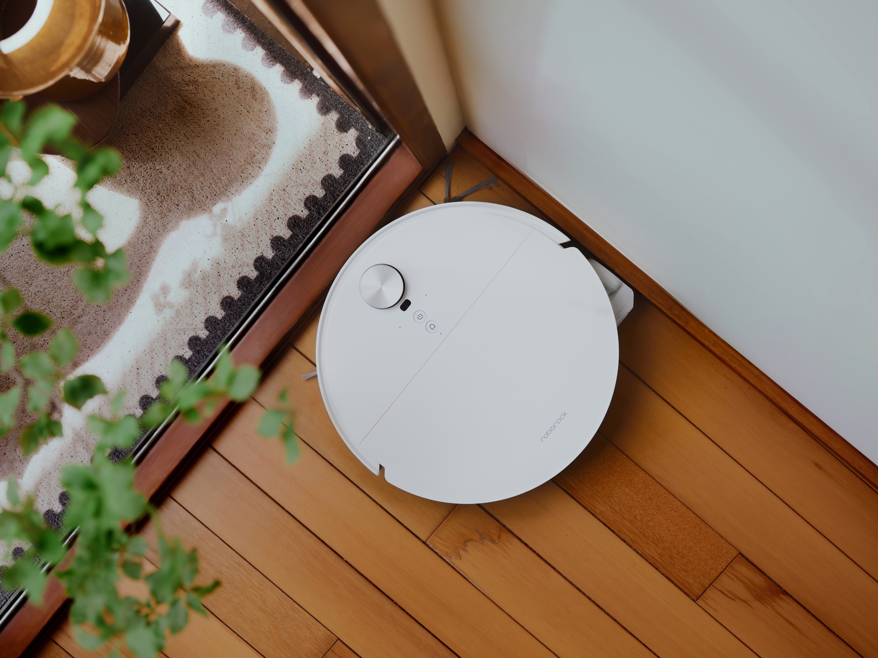 Weißer Roborock Saros 20 Flow Complete fährt neben einem Teppich über einen Holzboden