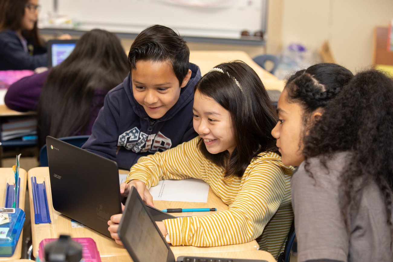 Schülerinnen und Schüler arbeiten im Klassenraum gemeinsam an einem Notebook - Bild: Google