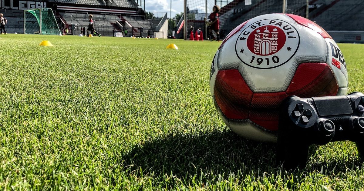 Fußball mit Vereinswappen des FC St. Pauli und PlayStation-Controller auf dem Rasen im Millerntor-Stadion - Bild: FC St. Pauli Rabauken